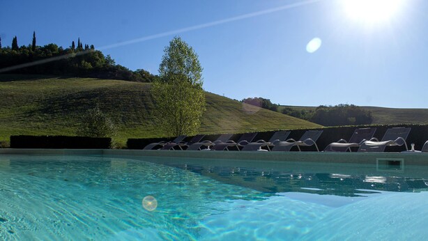 Une piscine à l’eau claire, entourée de chaises longues et avec une colline en arrière-plan.