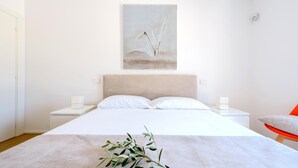 A minimalist bedroom with a large bed, two bedside tables, a modern headboard, and a single abstract painting on the wall. - Ecovilla Terra Di Luce 8 Emma Villas (Martina Franca)