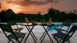 A poolside table with two chairs, two glasses of wine, and a plate of food. - Ecovilla Terra Di Luce 8 Emma Villas (Martina Franca)