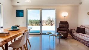 A modern living room with a wooden dining table, a brown leather armchair, a patterned sofa, and a glass coffee table. - Ecovilla Terra Di Luce 8 Emma Villas (Martina Franca)