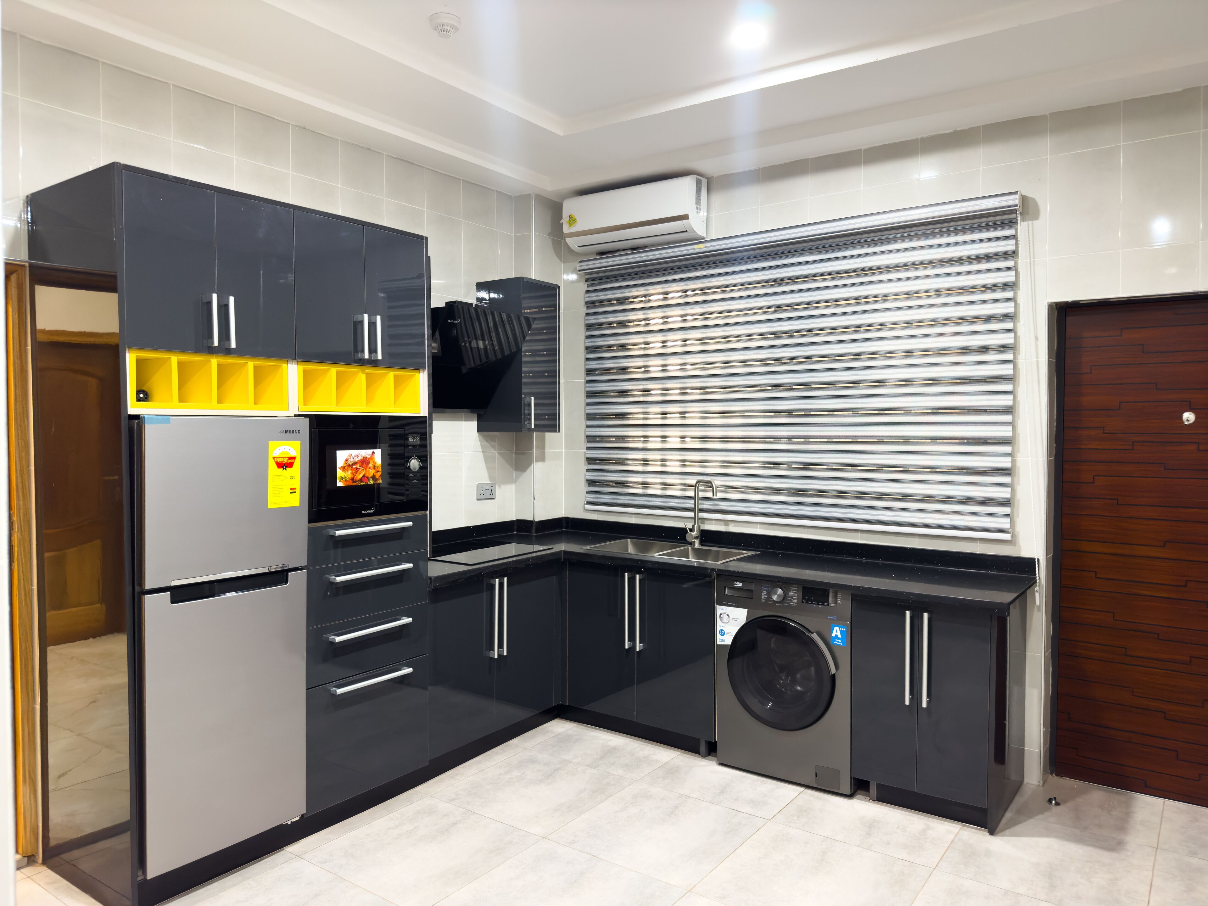 A modern kitchen with a built-in washer and dryer, a stainless steel sink, and a black and yellow refrigerator.