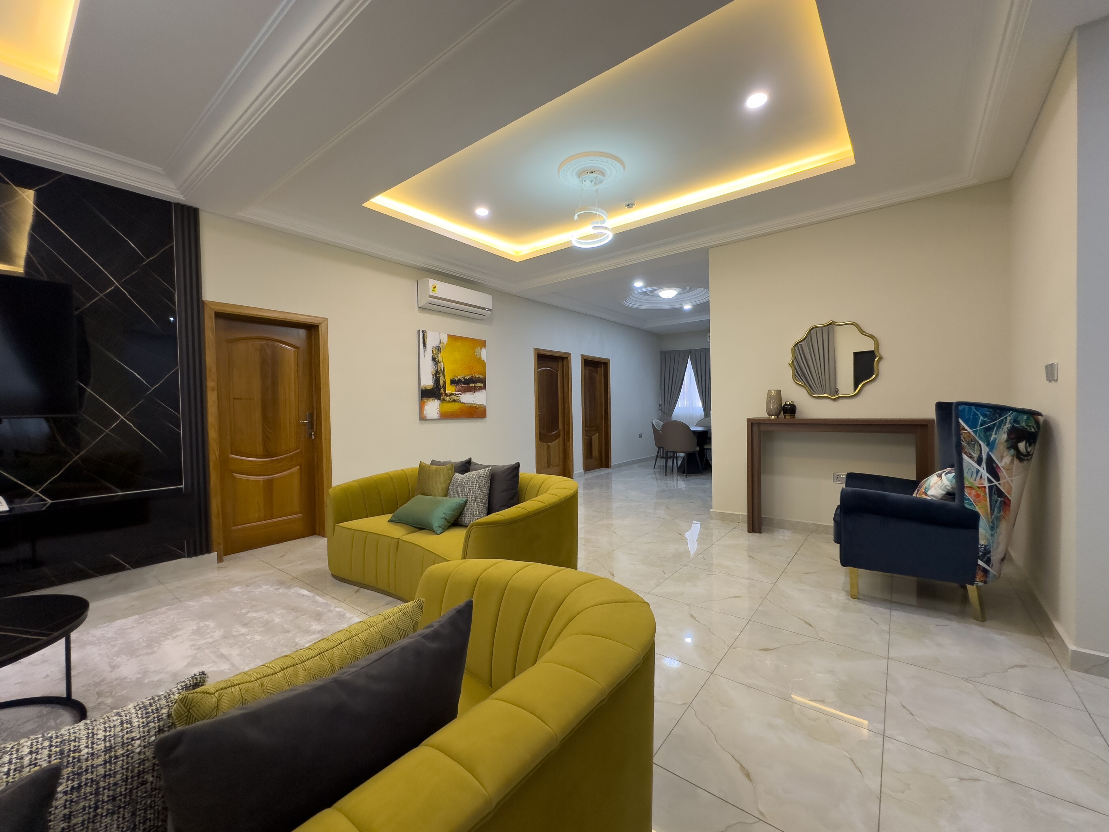 A spacious living room with a yellow sofa, a TV, and a dining area in the background.