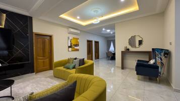 A spacious living room with a yellow sofa, a TV, and a dining area in the background.