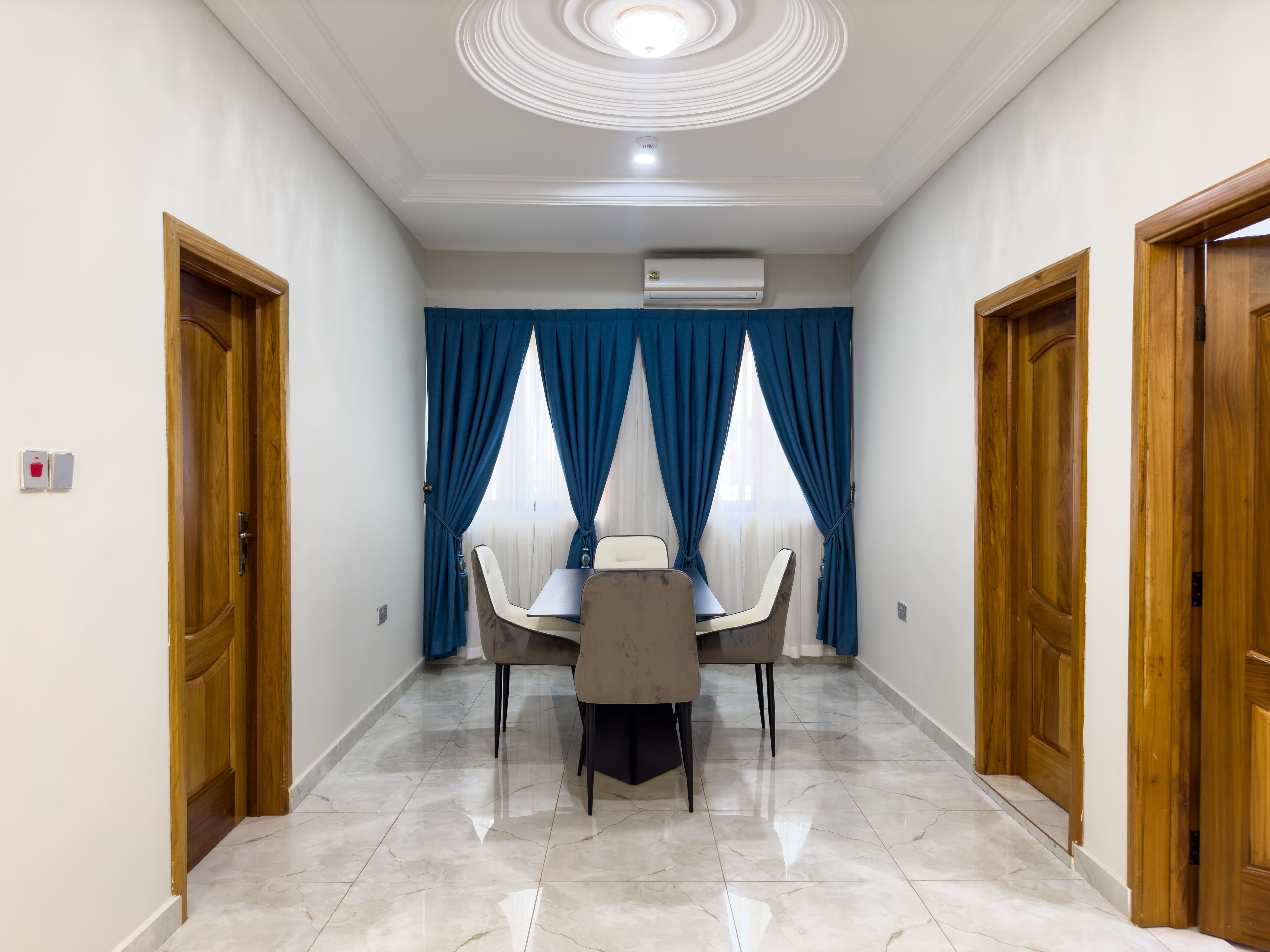 A hotel room with a dining area featuring a table and chairs, a ceiling light, and an air conditioning unit.