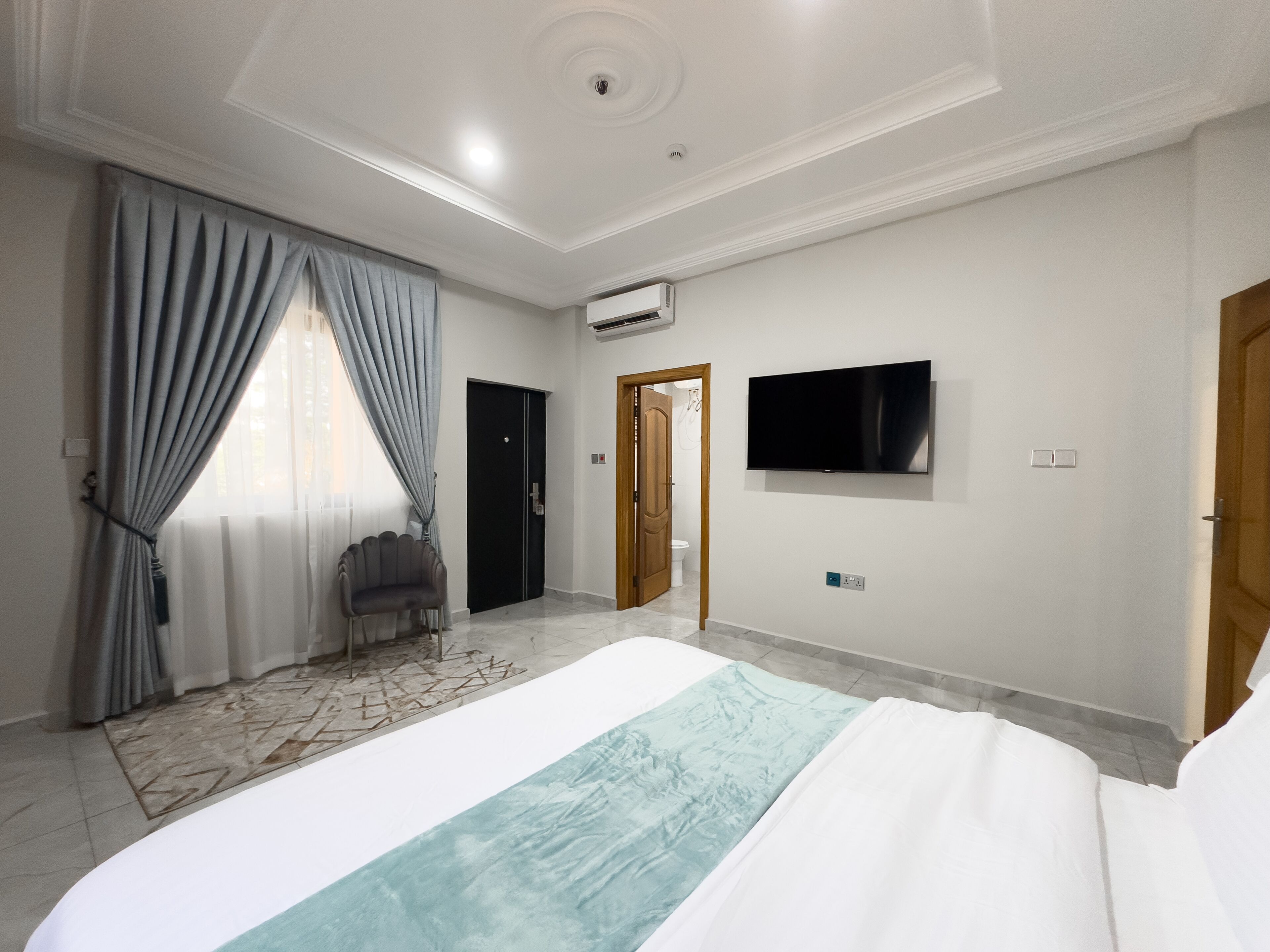 Une chambre d’hôtel avec un lit, une télévision, une porte et une fenêtre avec des rideaux.