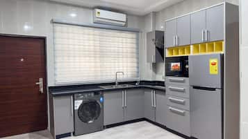 A modern kitchen with grey cabinets, a built-in washing machine, a stainless steel sink, and a grey refrigerator.