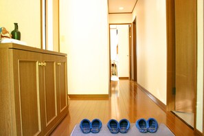 A hallway with wooden flooring, a set of blue slippers on a mat, and a cabinet with a green bottle on top.
