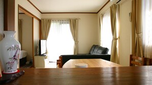 A room with a wooden dining table, a sofa, a television, and a large vase. - Lake Yamanaka Resort House II (Yamanakako)