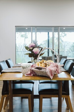 A dining table with chairs, a vase with flowers, and a basket of bread. - Wallaby 2 Bed, 1 Bath Cottage - Private Parkland Setting with Lake View (North Maleny)
