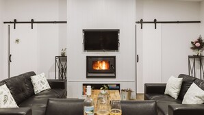 A modern living room with a fireplace, leather sofas, a wooden coffee table, and a flat-screen TV. - Wallaby 2 Bed, 1 Bath Cottage - Private Parkland Setting with Lake View (North Maleny)