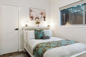 A bedroom with a bed, a window, a door, and a wall-mounted artwork. - Wallaby 2 Bed, 1 Bath Cottage - Private Parkland Setting with Lake View (North Maleny)