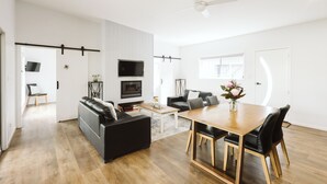 A modern living room with a sofa, dining table, and TV. - Wallaby 2 Bed, 1 Bath Cottage - Private Parkland Setting with Lake View (North Maleny)