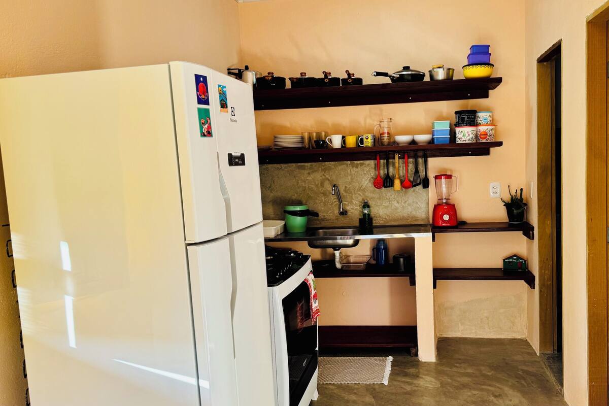 Een kleine keuken met een koelkast, fornuis, spoelbak en diverse keukenattributen en apparaten.