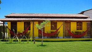 Um edifício amarelo com telhado de azulejos, uma rede e uma pequena árvore no jardim da frente.