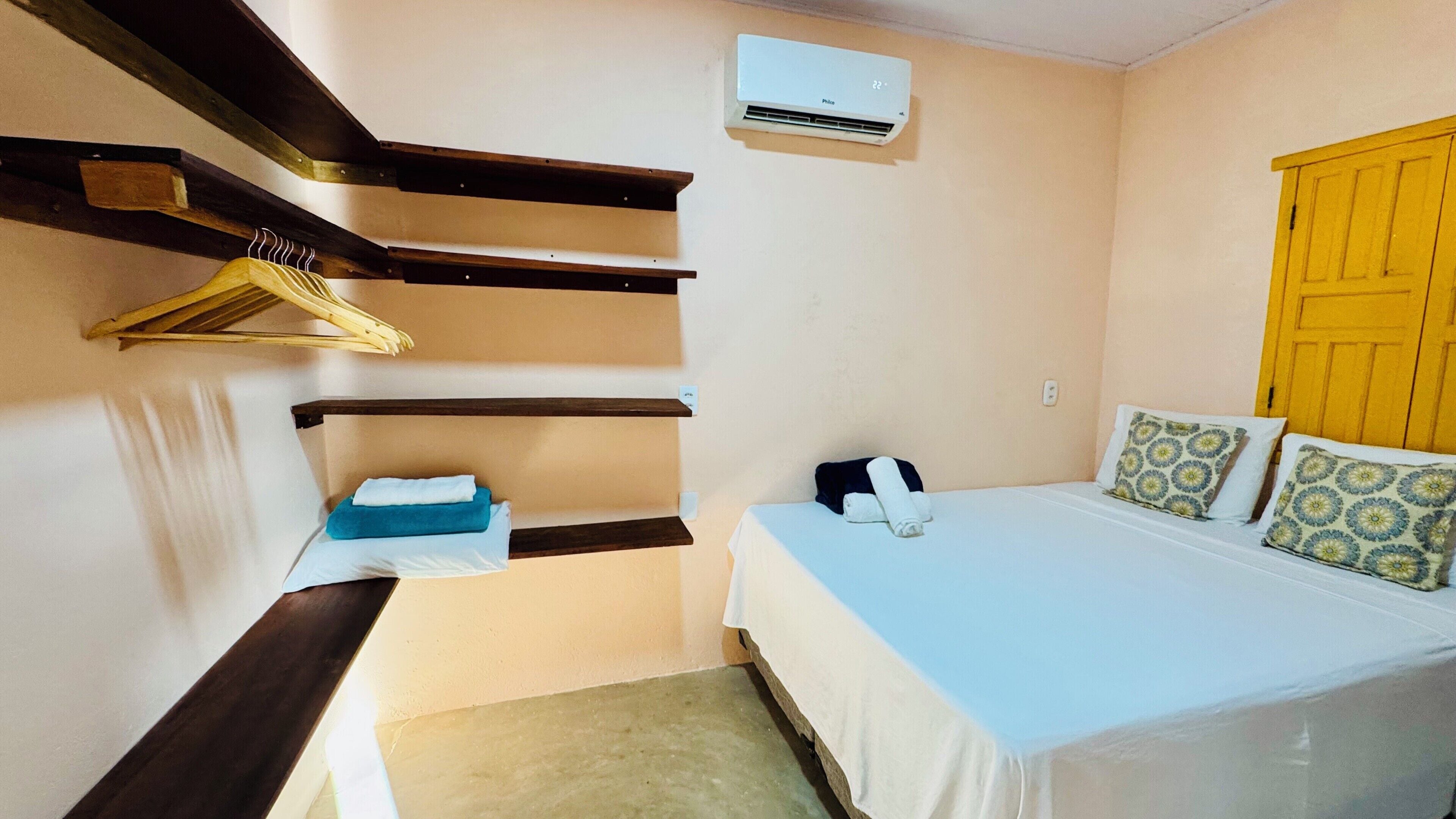 Un dormitorio con cama, un perchero, aire acondicionado instalado en la pared y una puerta amarilla.