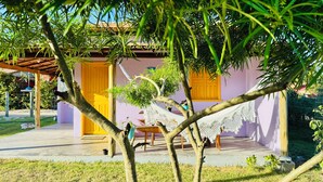 Uma casa com porta de madeira, rede e mesa na varanda.