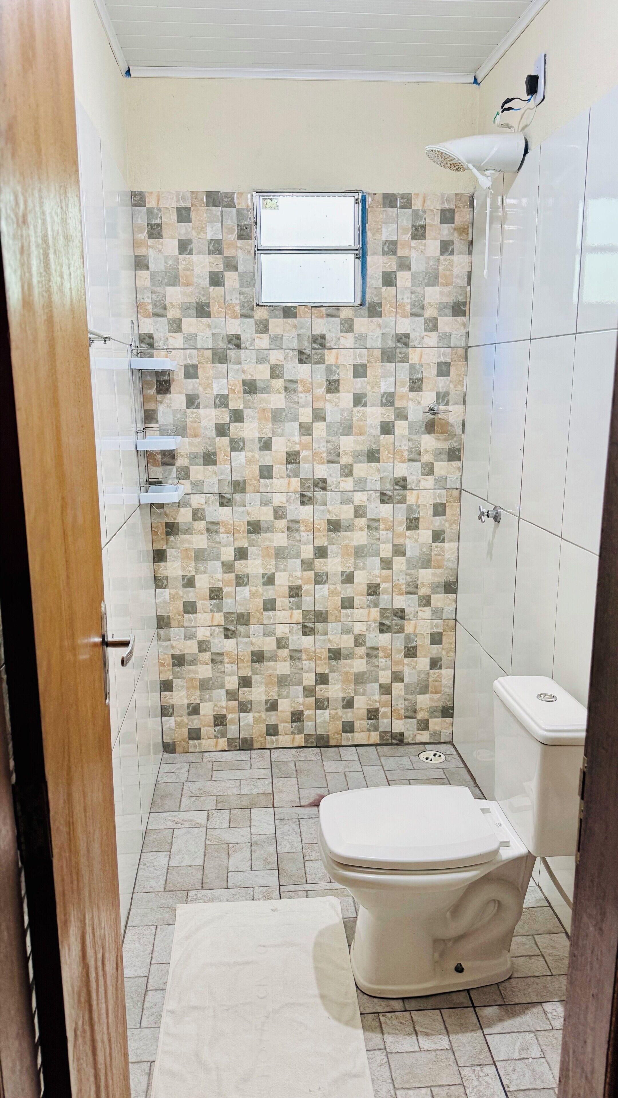 A bathroom with a tiled shower wall, a toilet, and a small window.