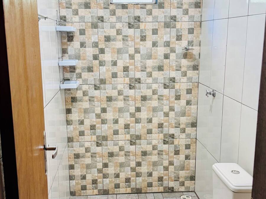 A bathroom with a tiled shower wall, a toilet, and a small window.