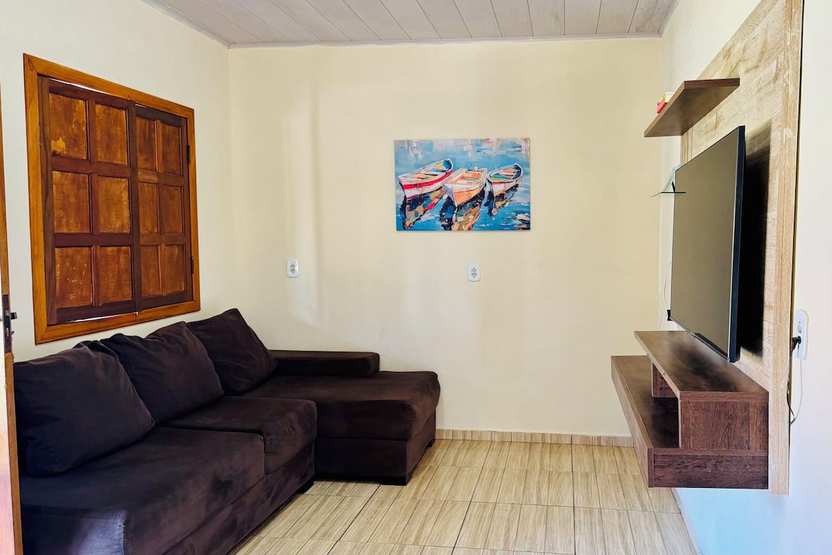 Een woonkamer met een donkerbruine hoekbank, een wandgemonteerde flatscreen-tv, een houten plank en een schilderij van boten aan de muur.