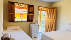 Quarto com duas camas, um pequeno frigorífico e janela com vista para um edifício.
