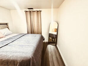 Ein Schlafzimmer mit Bett, Vorhängen, einem Spiegel und Holzboden.