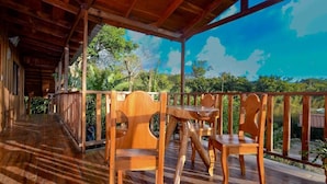 A wooden deck with a table and chairs, surrounded by a wooden railing, overlooking a lush green landscape.