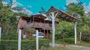 A wooden house with a balcony, surrounded by lush greenery and a clear sky.