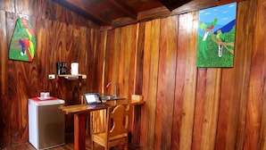 A wooden-paneled room with a small desk, a laptop, a refrigerator, and a chair.