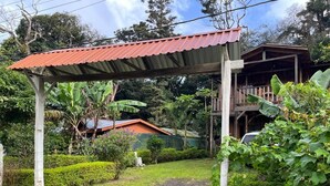 A covered outdoor area with a wooden structure, a dirt path, and lush greenery.