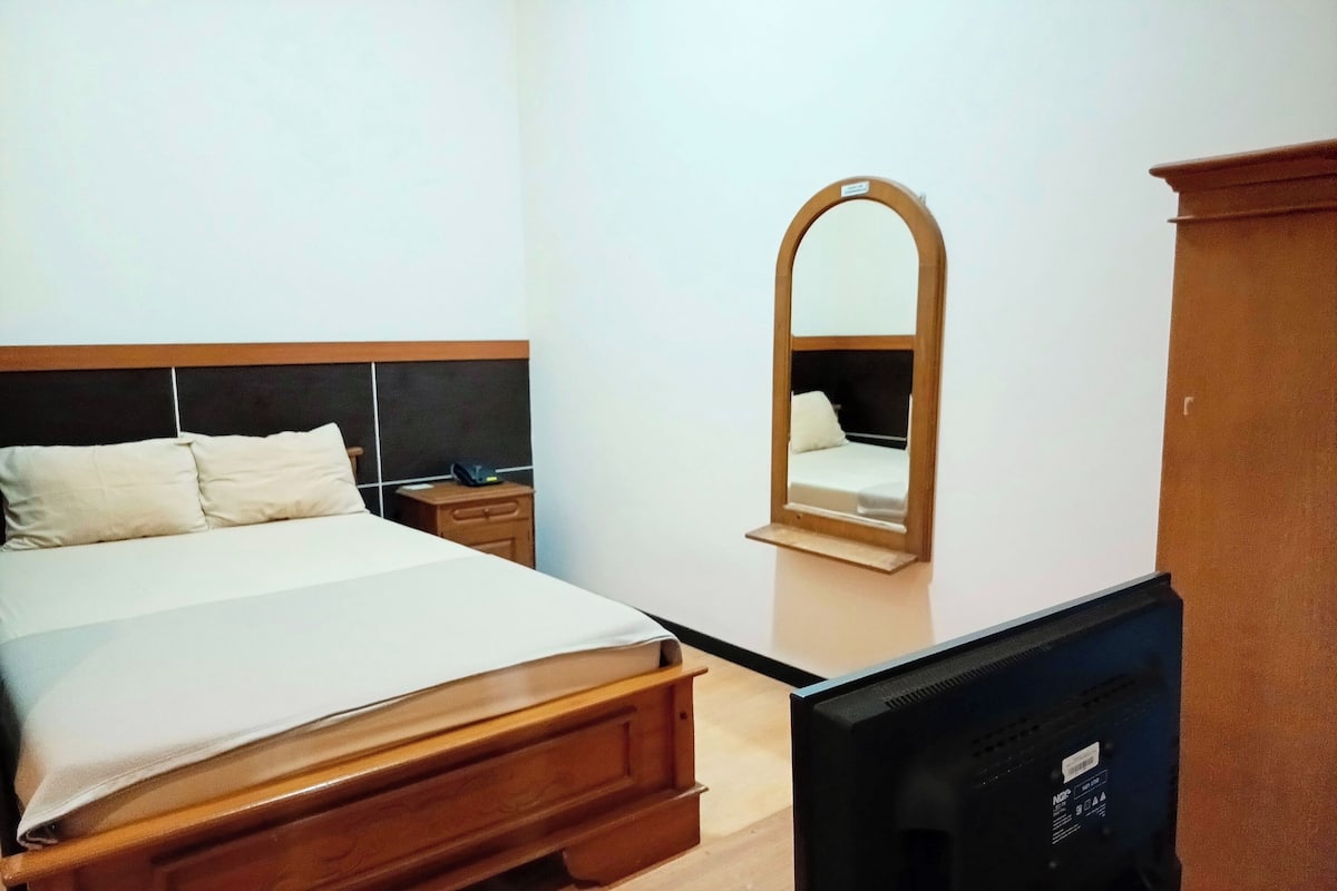 A hotel room with a bed, a nightstand, a mirror, and a television.