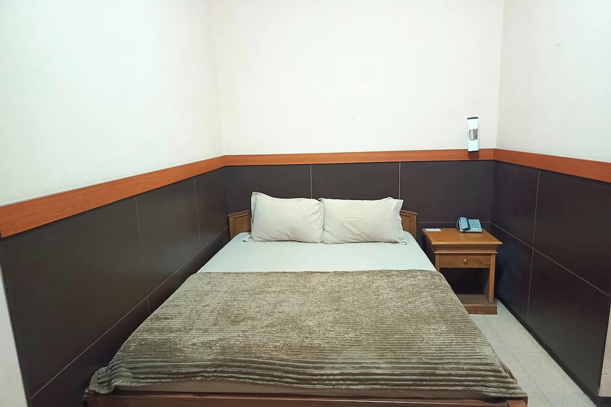 A small, neatly made bed with a wooden headboard and a single bedside table with a phone and a lamp.