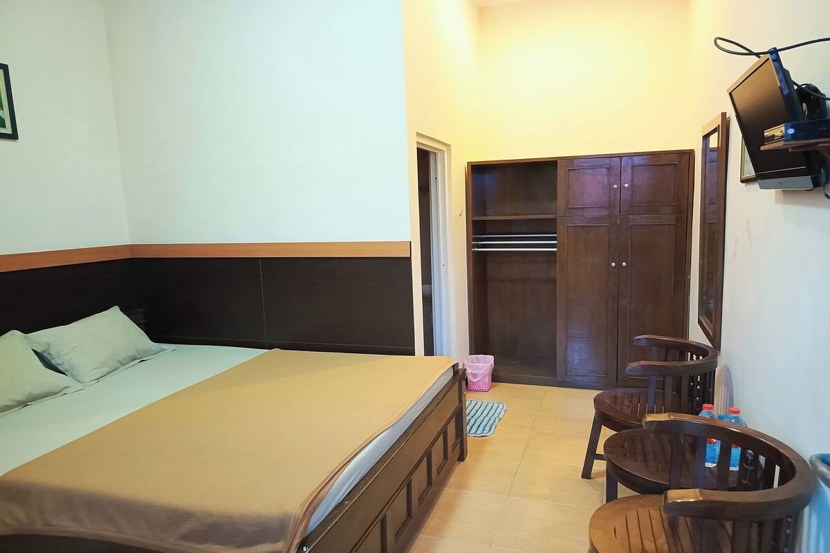 A bedroom with a bed, a desk, and a chair. There is a wardrobe and a television mounted on the wall.