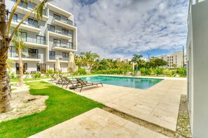 A modern building with a swimming pool, outdoor seating, and greenery.