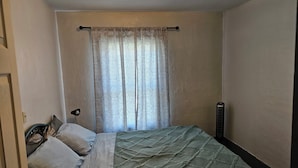 Ein Schlafzimmer mit einem Bett, einem Fenster mit Vorhängen, einem Heizkörper und einer Wandleuchte.