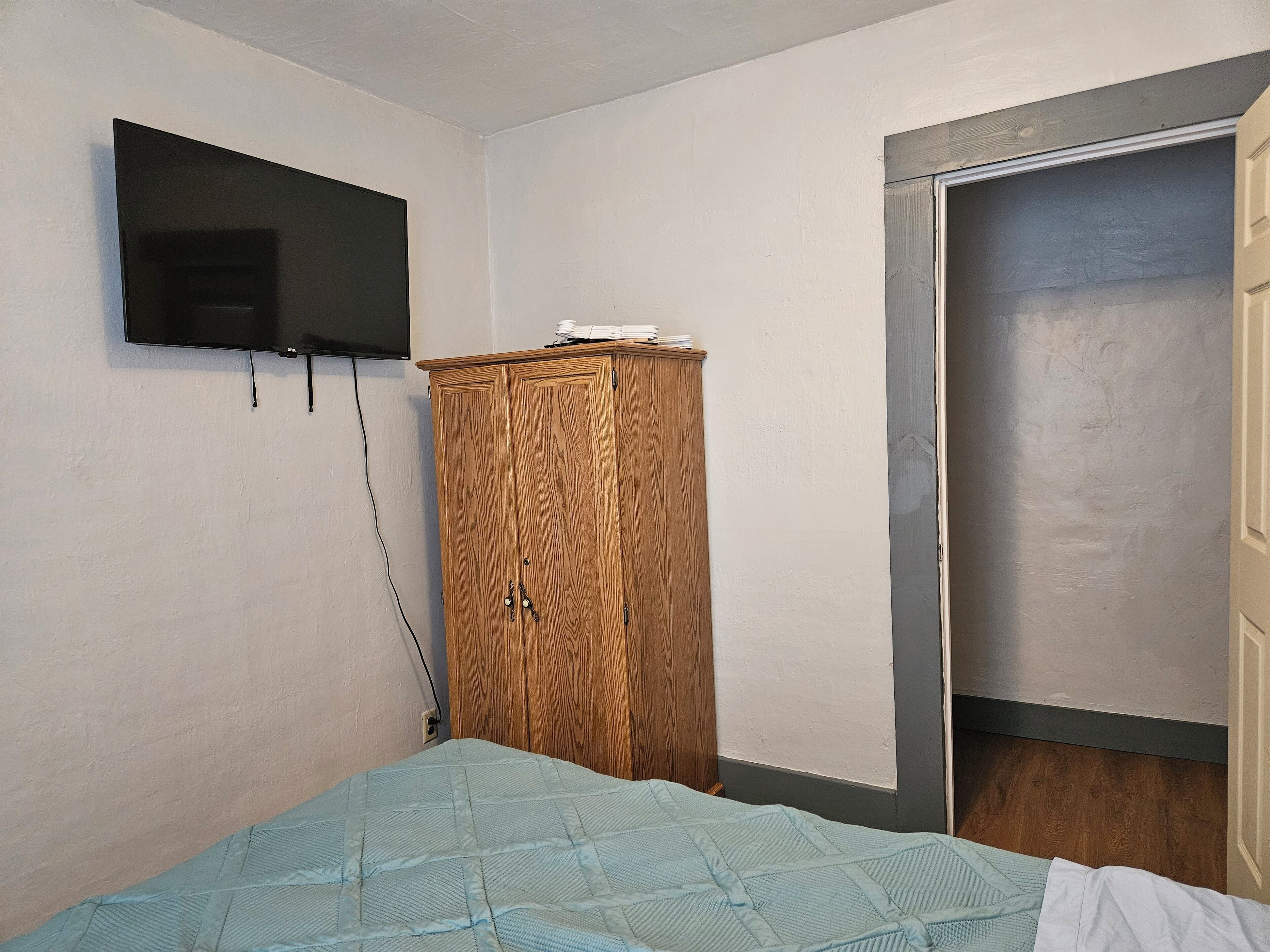 A bedroom with a bed, a wooden wardrobe, a television mounted on the wall, and a door.