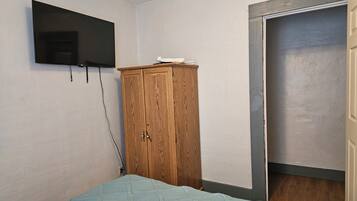 A bedroom with a bed, a wooden wardrobe, a television mounted on the wall, and a door.