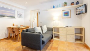 Una sala de estar acogedora con un sofá, una mesa de comedor con sillas, un televisor montado en la pared y un escritorio pequeño con cajones.