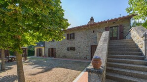 A stone building with a red-tiled roof, a wooden staircase, and a garden area with a tree and a bench. - Beautiful private villa with private pool, WIFI, terrace, pets allowed and panoramic view (Cortona)