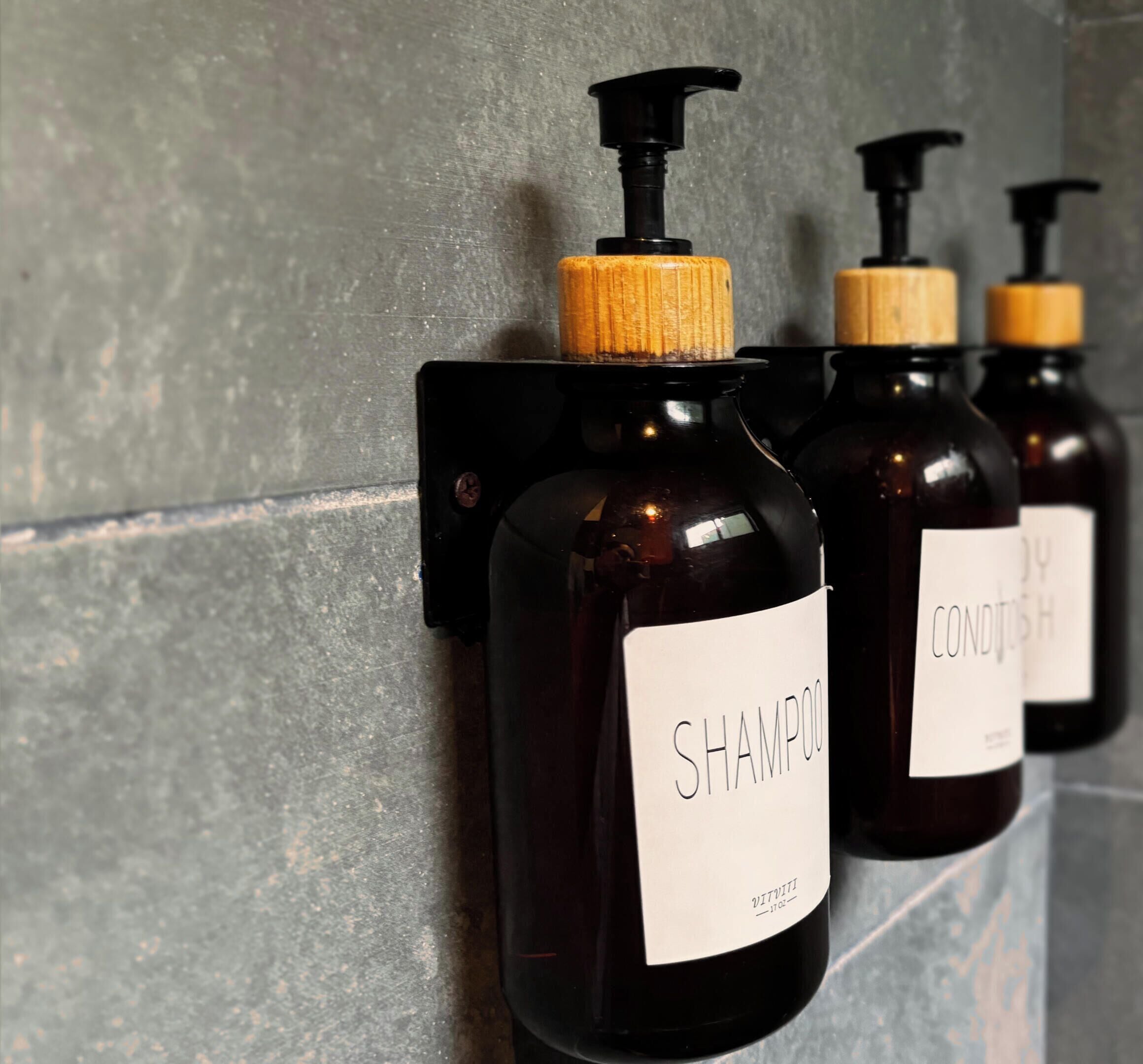 Tres botellas de champú y acondicionador sujetas a una pared.