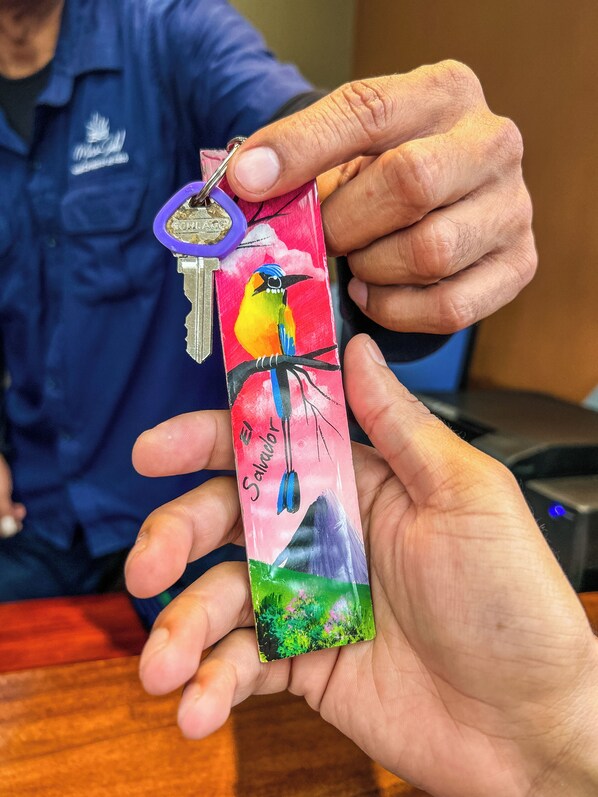 A hand holding a keychain with a colorful bird illustration and the word "Salvador" on it.