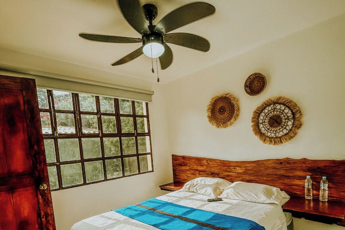 A bedroom with a bed, a ceiling fan, a window, and wall decorations.