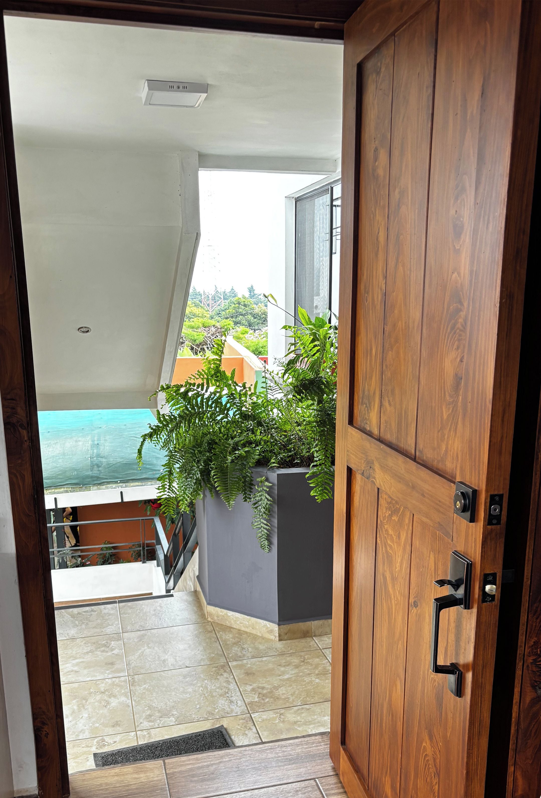 Uma porta de madeira dá para uma varanda com vista para uma piscina e áreas verdes.