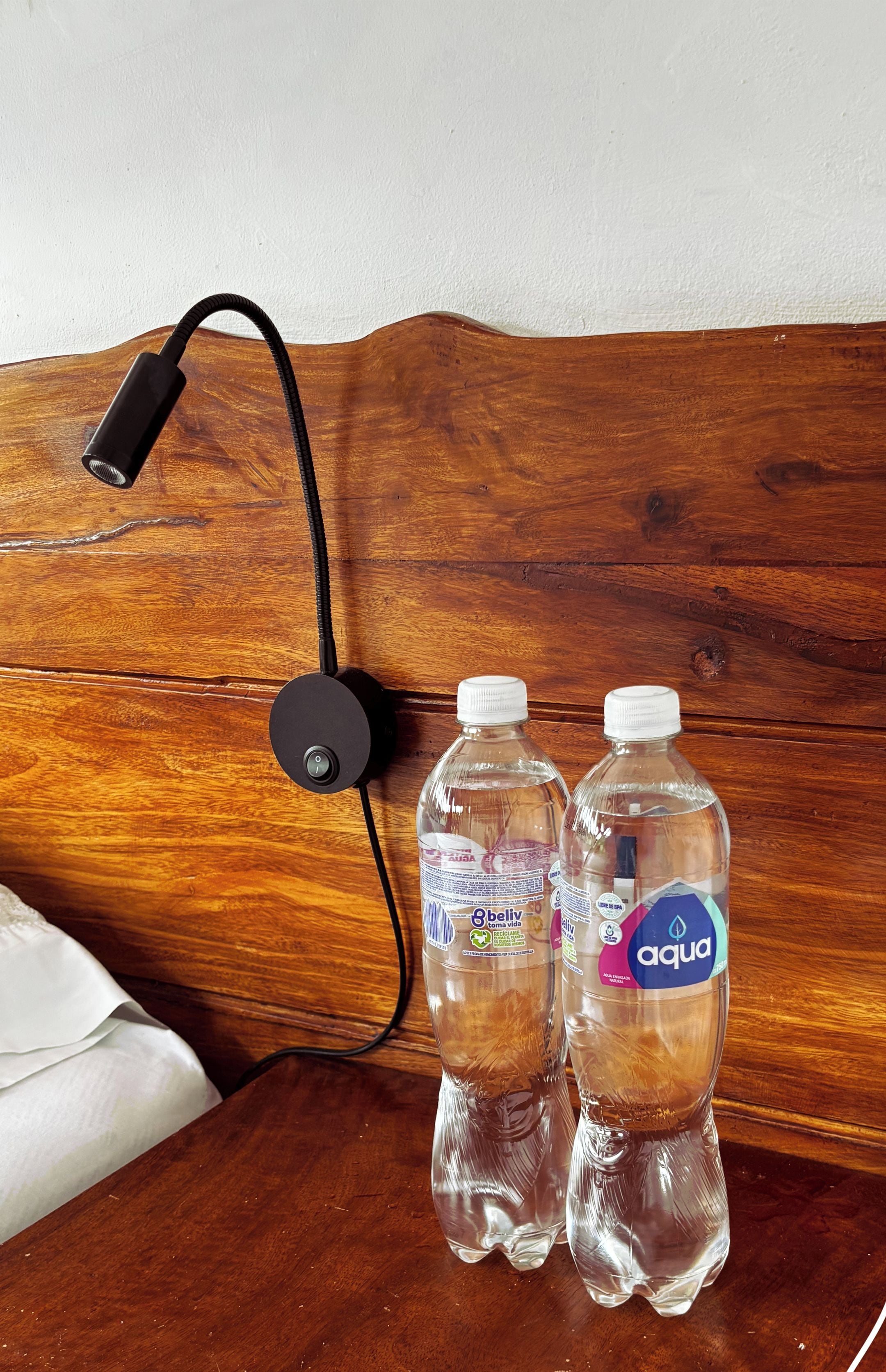 A wooden headboard with a power outlet and two water bottles labeled 'beliv' and 'aqua'.