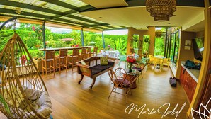 A spacious outdoor area with a wooden floor, wicker furniture, and a hanging chair. - Hotel Maria Isabel Ataco (Jujutla)