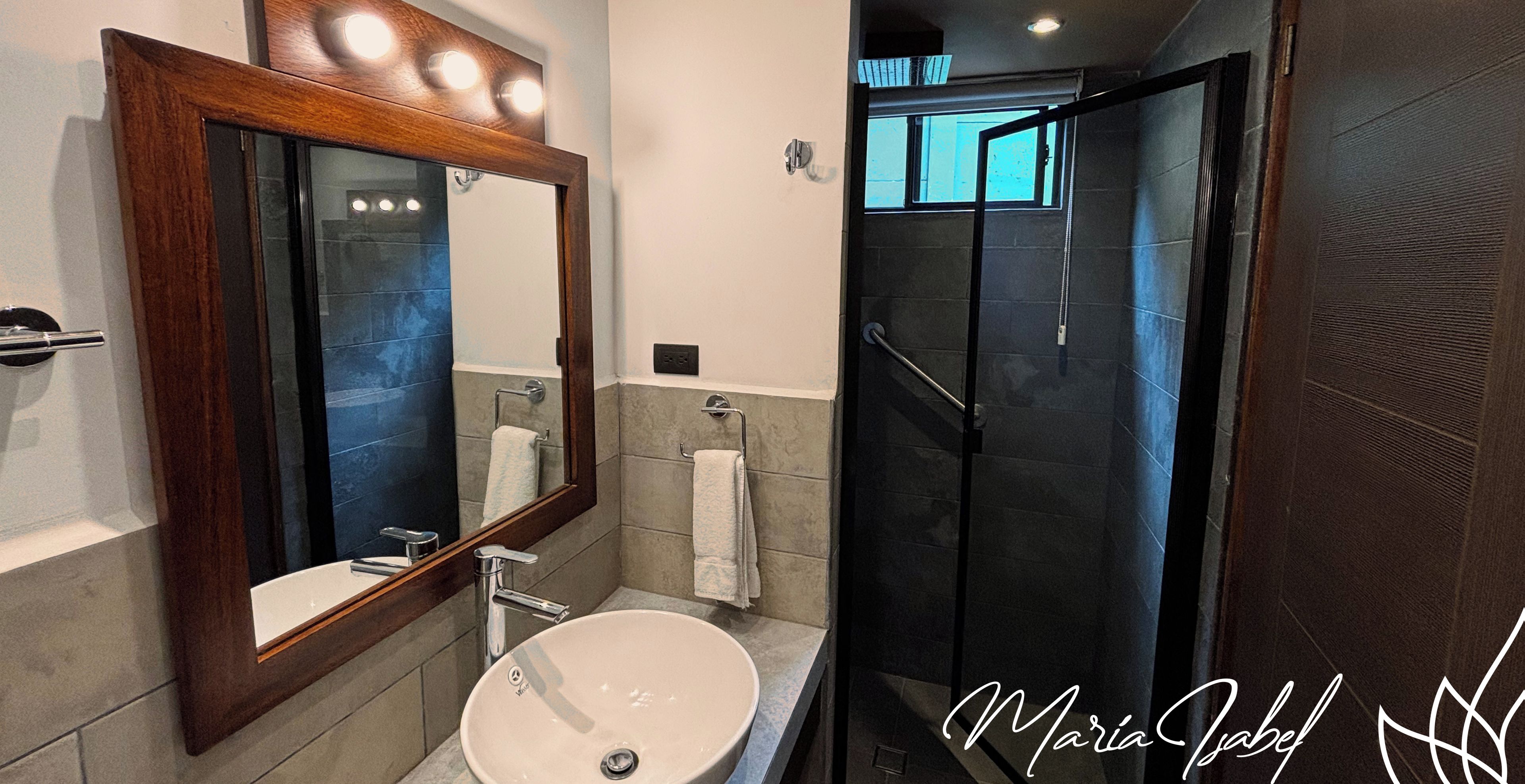 A modern bathroom with a large mirror, a sink, and a walk-in shower.