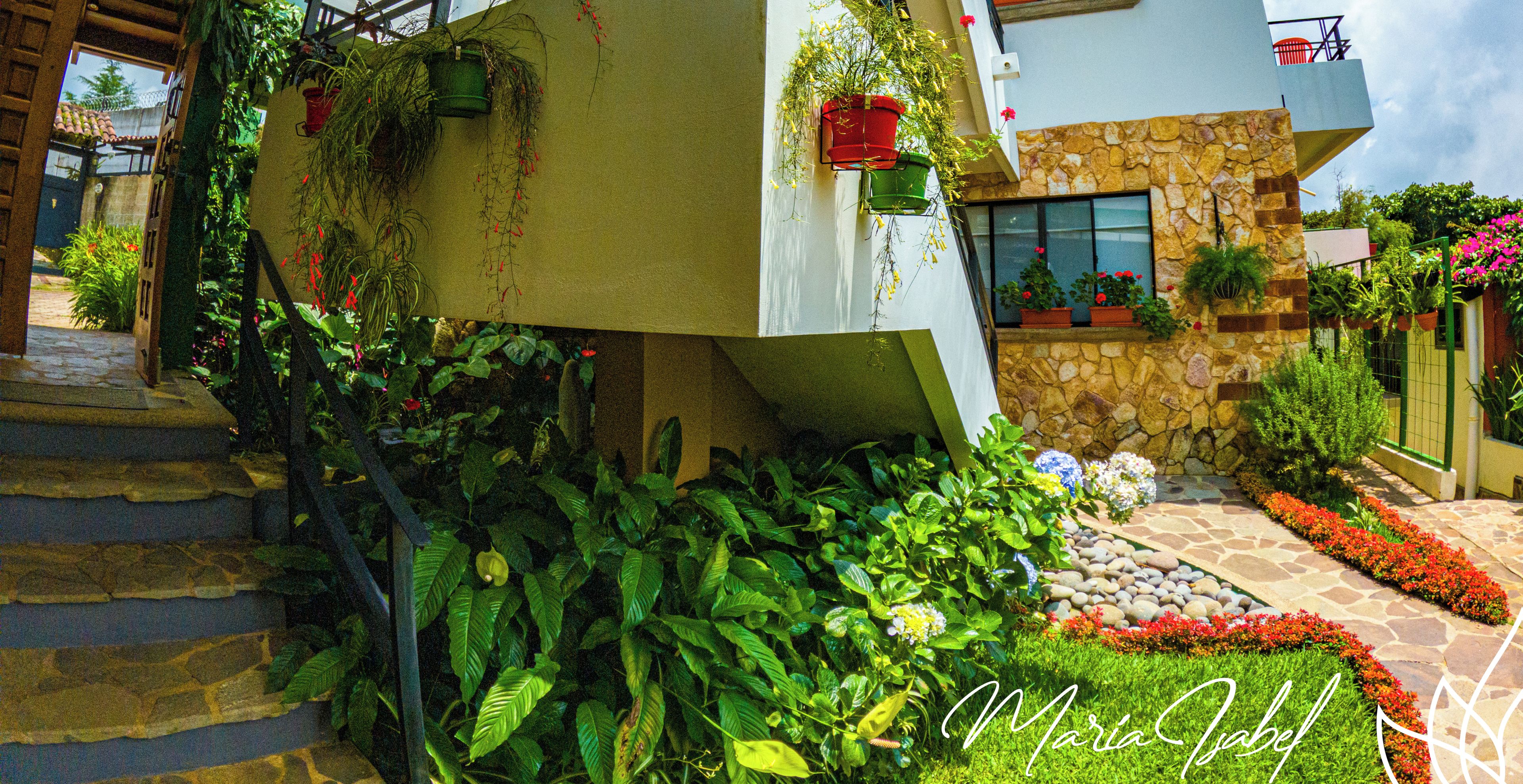Ein modernes Hotel mit Natursteinfassade, ein gepflegter Garten mit verschiedenen Pflanzen und Blumen sowie eine Treppe zum Eingang.