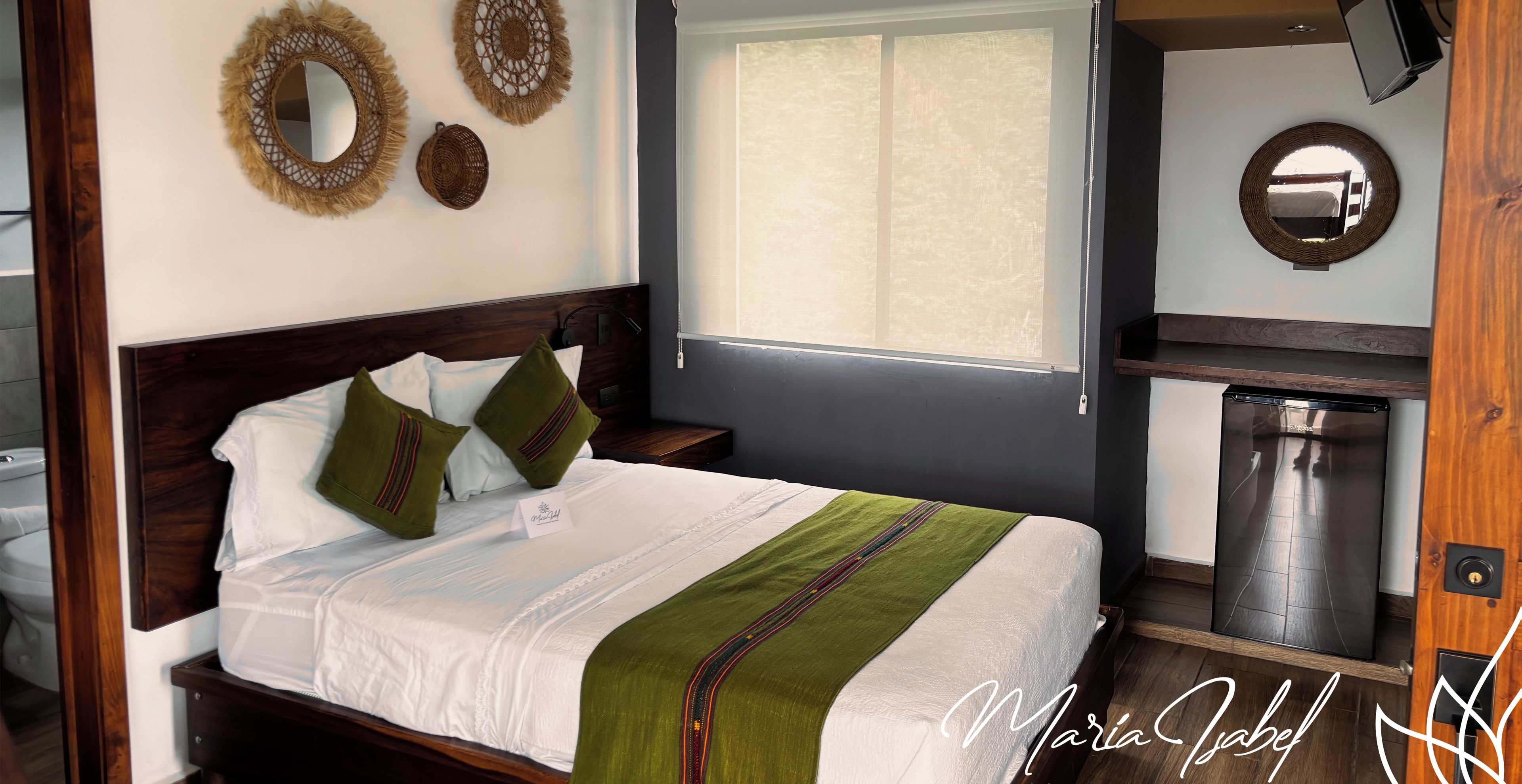 A neatly made bed with a green throw, a wooden headboard, and two decorative wall mirrors.