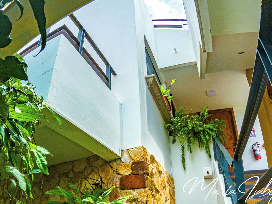 Interior de hotel com parede de pedra, escadaria e plantas.