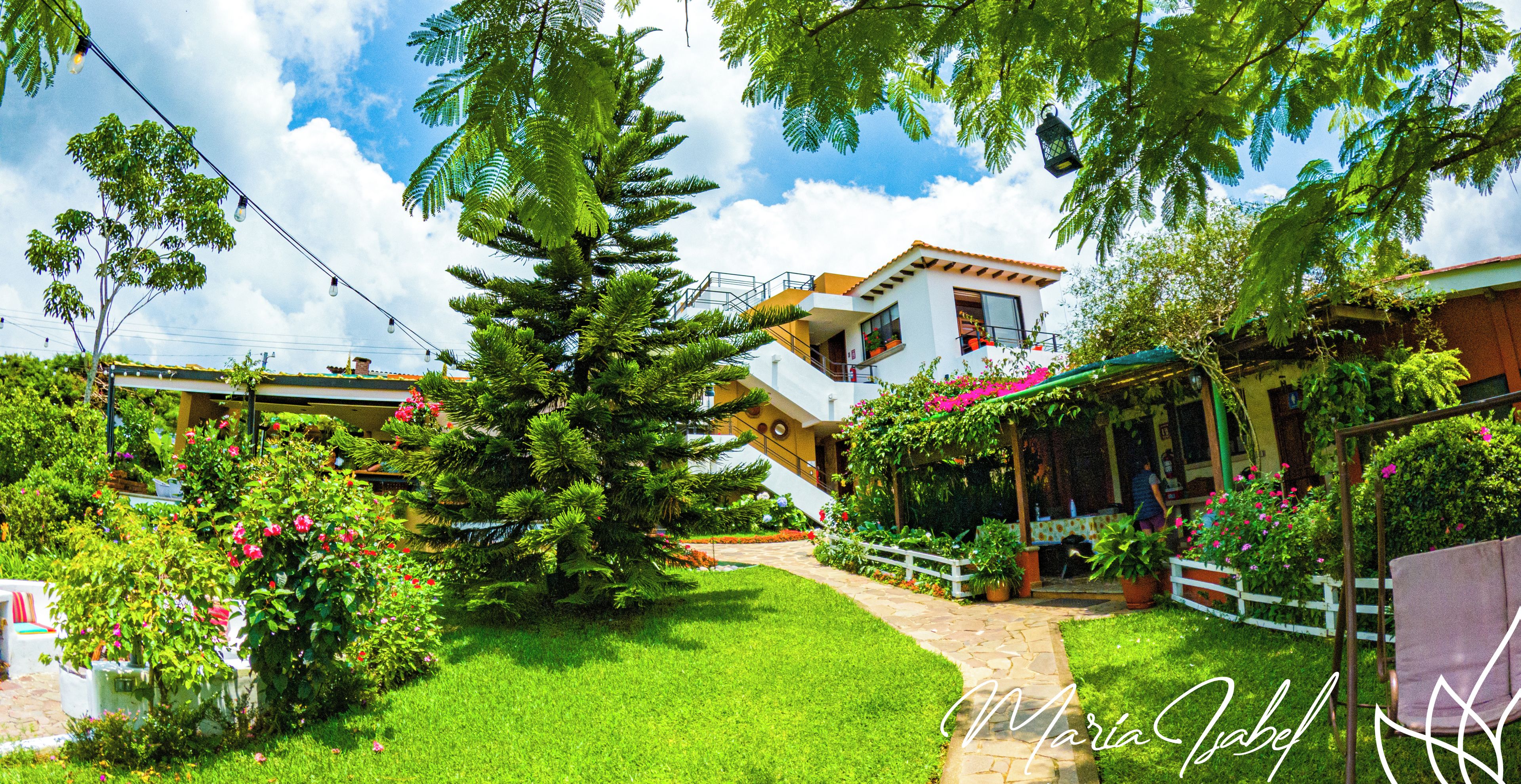 Um hotel com um jardim bem cuidado, uma área de estar coberta ao ar livre e uma escadaria que leva aos andares superiores.