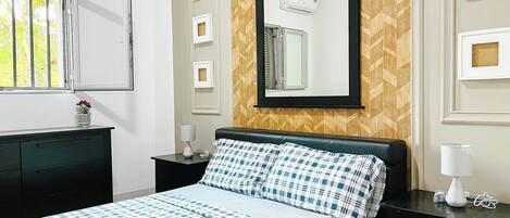 A neatly arranged bedroom with a bed, a dresser, a nightstand, and a mirror.